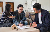 Asian couple looking at house plans and talking with a real estate agent about signing documents for purchase of a new home.