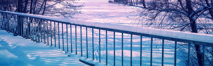 Bridge over a frozen river in the park in winter. Horizontal banner