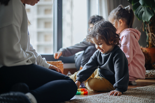 Happy mother and little daughter playing with toy dinosaurs close up, sitting on warm floor with underfloor heating, smiling dad and overjoyed girl child enjoying leisure time at home together