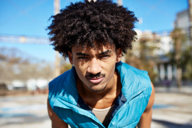 Head and shoulders portrait of 21 year old wearing blue ski vest, bending over to get a good look, serious expression, bright sunshine.