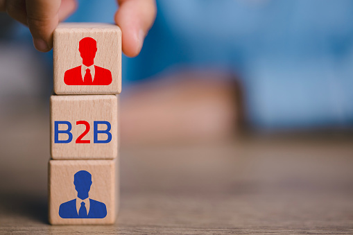 A person is holding three wooden blocks with two men on them and the letters B2B. The blocks are stacked on top of each other