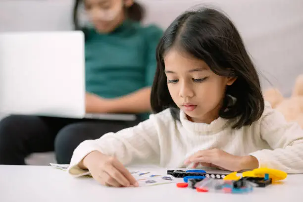 Photo of A young girl is sitting at a table with a laptop and a stack of Legos
