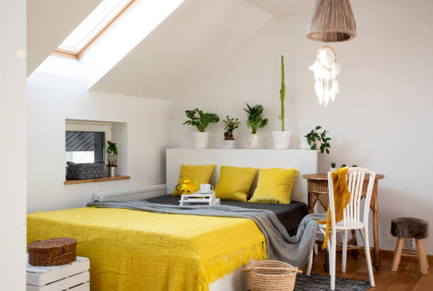 Home decor in cosy bedroom with bed, wooden floor and boho yellow decoration. Interior decor in the attic. Cosy white comfort room with bed with yellow blanket and pillow, plant and window in the attic. Decorating architecture. Home interior. modern cottage interior design stock pictures, royalty-free photos & images