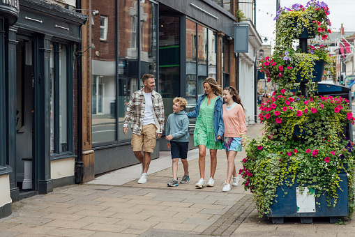 Wide shot of a family of four walking down the street on a day out. The family consists of a mother and father, son and daughter. They are all smiling while walking through the streets of Morpeth in the North East of England.\n\nVideos are available similar to this scenario.