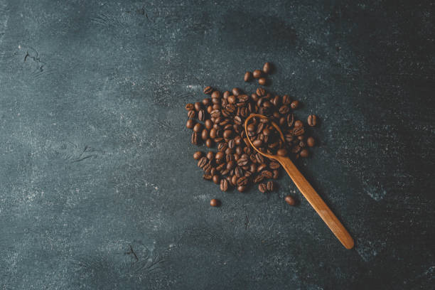 istock Coffee beans pour out from a wooden spoon on a retro background, top view 2119548340