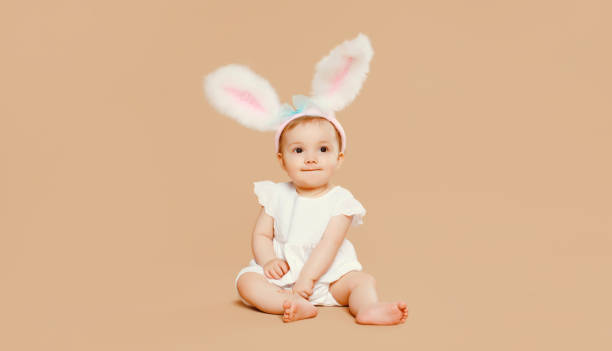istock Portrait cute baby with easter rabbit ears sitting on brown studio background 2119557326