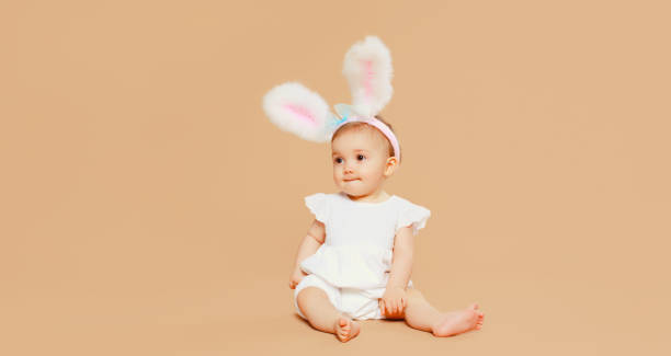 istock Portrait cute baby with easter rabbit ears sitting on brown studio background 2119557702