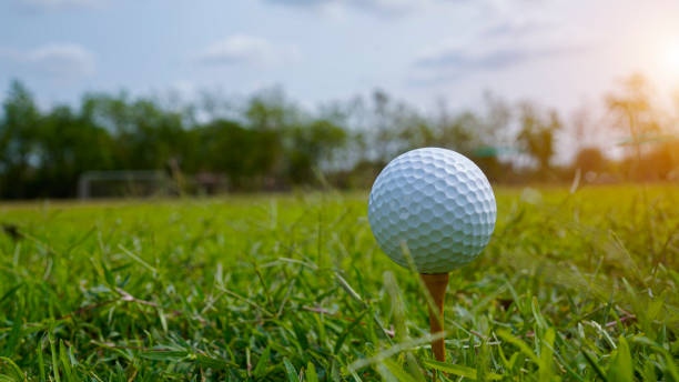 istock golf ball on tee in beautiful golf course with sunset. 2119607484