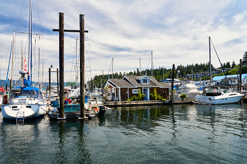 Cowichan Bay, Canada – June 08, 2023: A float home at Cowichan Bay Marina amongst the pleasure boats moored at the dock on a bright summer day.
