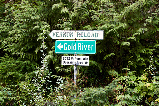 A directional sign surrounded by dense trees indicating the way to Gold River and Vernon Reload logging operations.