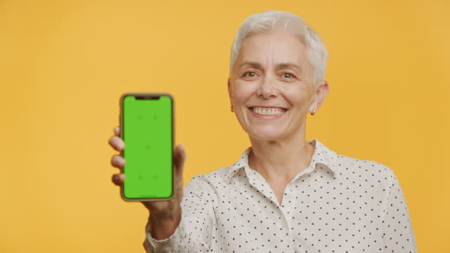 Smiling Senior Woman Presenting Smartphone with Green Screen