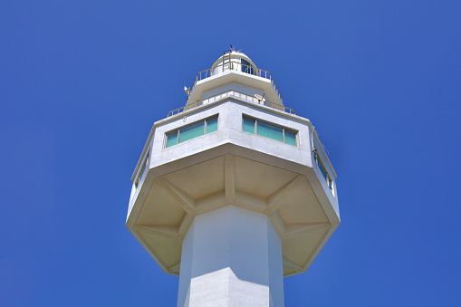 Goseong County, South Korea - July 31, 2019: Looking up from its base, the towering white Daejin Lighthouse reaches into the blue sky, its octagonal structure standing 31 meters tall, a beacon of guidance and beauty on the coast.