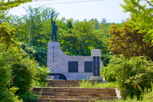 Goseong County, South Korea - July 31, 2019: Near the reception building of the Goseong Unification Observatory, a statue stands on a granite pedestal, depicting a man holding a torch aloft, symbolizing hope for the reunification of Korea, accompanied by plaques echoing the same aspiration.