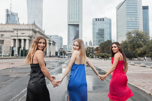 Happy beautiful fashion girls girlfriends in stylish elegant dresses walk in the city and go to a party, back view
