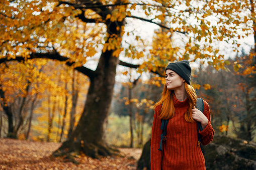 woman in a sweater walks in the park in autumn nature landscape fresh air Model backpack. High quality photo