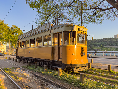 PORTO, PORTUGAL - 5 APRIL 2023: Wooden historical vintage yellow tram 287 moving on Porto street, symbol of city.Old tram passing by in Massarelos with the Arrabida bridge in the background during sunset. Indispensable transport for locals and interesting attraction for tourists. Portugal