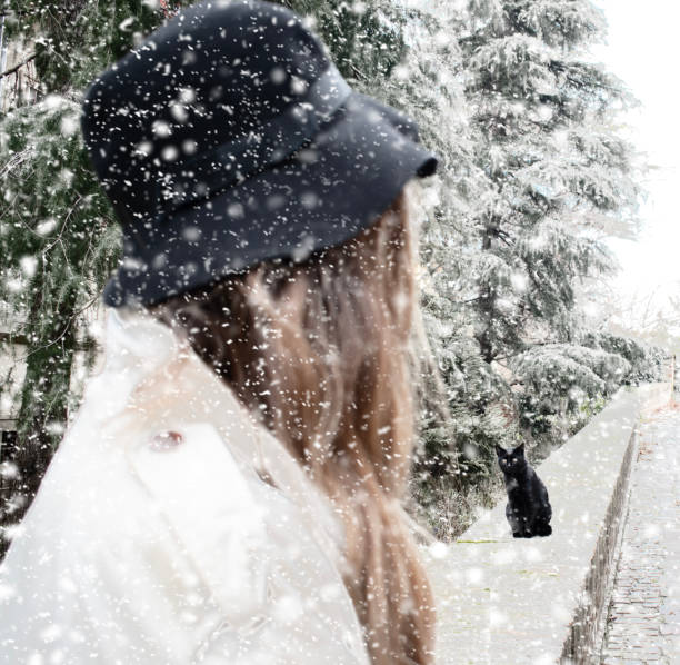 Girl with hat loking at the cat when it is snow