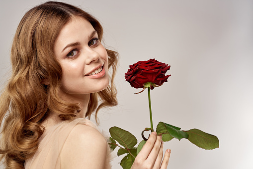 Charming woman with a red rose in her hands on a light background portrait close-up cropped view. High quality photo