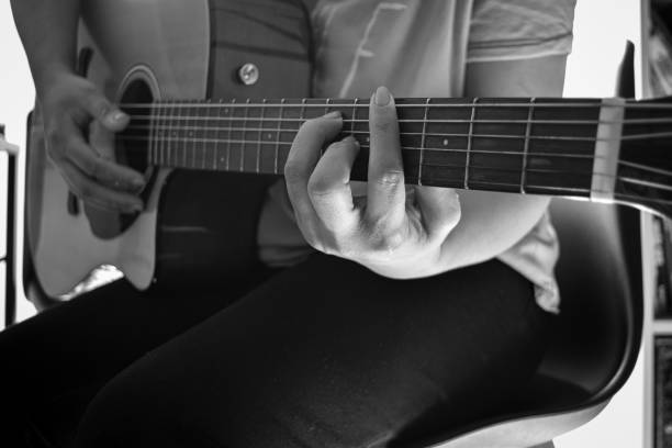 A female is sitting and playing an acoustic guitar