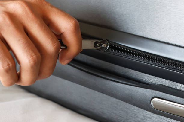 istock Full frame image of grey wheelie suitcase on double bed covered by white duvet, unrecognisable person zipping up luggage, focus on foreground 2119756549