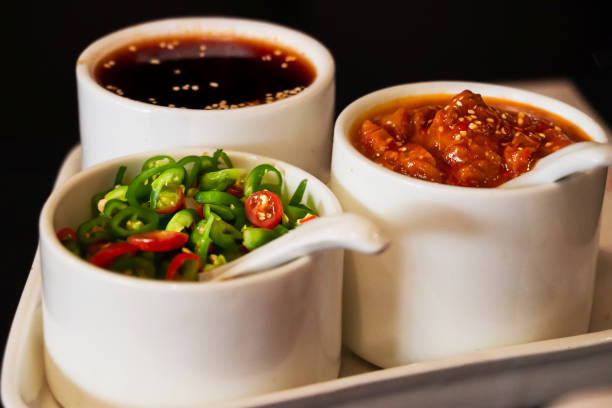 Stock photo showing close-up view of Chinese savoury dips and oils served in three, white, porcelain ramekins on a triangular tray.