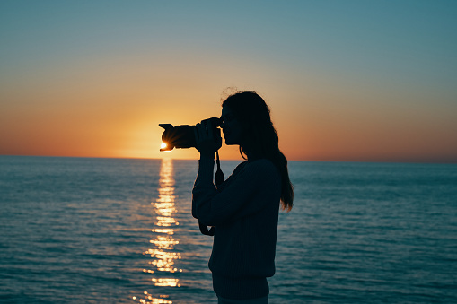 woman photographer with camera at sunset near the sea on the beach. High quality photo