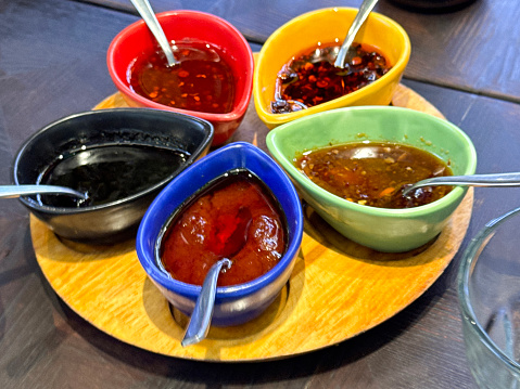 Stock photo showing close-up view of Chinese savoury dips and oils served in yellow, red, black, blue and green, teardrop porcelain oriental sauce boats as part of a buffet display.