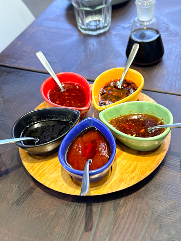 Stock photo showing close-up view of Chinese savoury dips and oils served in yellow, red, black, blue and green, teardrop porcelain oriental sauce boats as part of a buffet display.