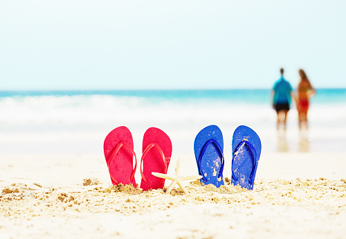 Pink and blue flip-flops on the beach. Copy space in the sky.
