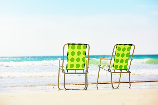 Two folding deckchairs side by side on a sunny beach, facing the ocean.