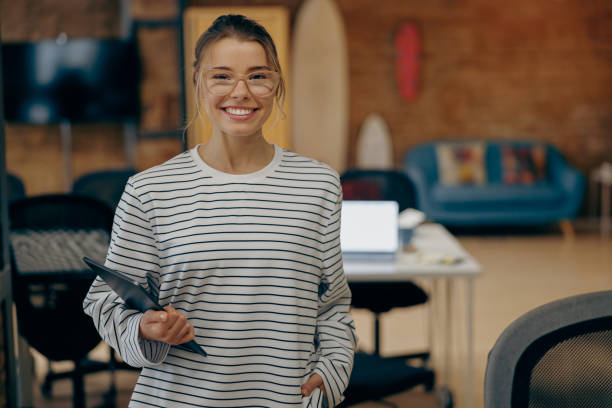 istock Smiling female manager holding digital tablet and looks camera standing on modern office background 2119782987