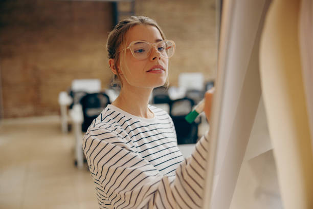 istock Concentrated female employee draws graph on the flipchart before presenting project on meeting 2119784519