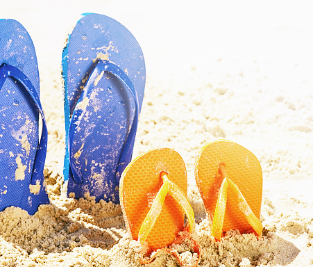 Adult and child footwear of different sizes on a sandy beach.