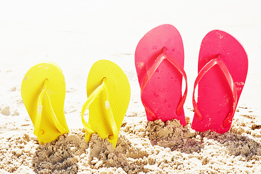 Adult and child footwear of different sizes on a sandy beach.