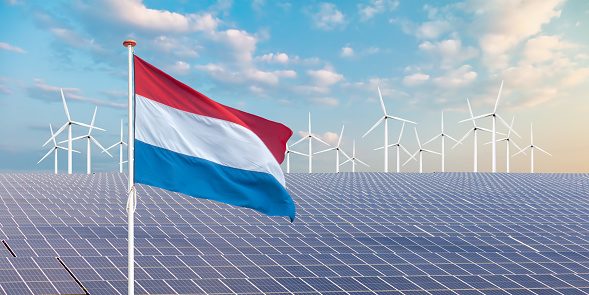 Official flag of The Netherlands in front of a large array of solar panels and wind turbines