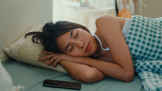 Young Asian woman with pajamas laying on convenience and comfort bed feel calm and relaxing in bedroom at home late morning. Sleep innovation concept.