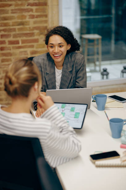 istock Two smiling female freelancers talking during work on laptop while sitting in cozy coworking 2119796177