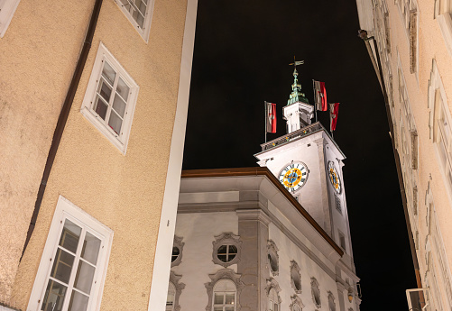 Salzburg, Austria, August 15, 2022. Fascinating night shot of the town hall clock tower. The red and white flags stand out.