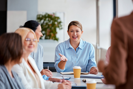 Smiling businesswoman sitting with colleagues during conference meeting in office