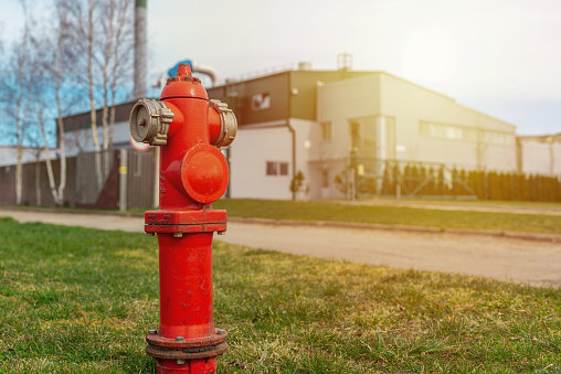 Single red fire hydrant on green sunset lawn.In a background factory.Autumn,spring,summer day.Copy space.