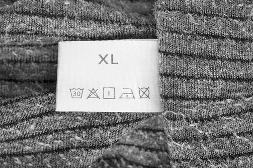 Size XL washing instructions clothes label on knit grey fabric closeup