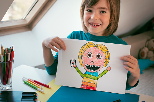 Cute smiling boy with missing teeth drawing a self-portrait