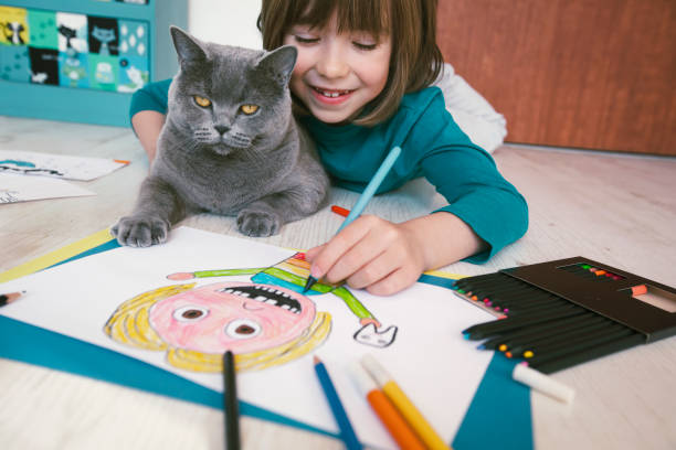 istock Cute boy with missing teeth drawing a self-portrait. Cat next to him 2119878192