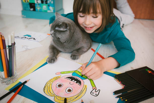 istock Cute boy with missing teeth drawing a self-portrait. Cat next to him 2119878718