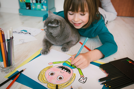 Cute smiling boy with missing teeth drawing a self-portrait. Cat next to him.