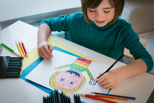 Cute smiling boy draws a portrait of a child with missing teeth.