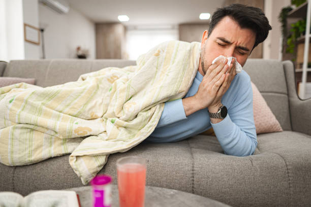 istock Sick man blowing his runny nose while lying on a sofa covered with blanket 2119883636