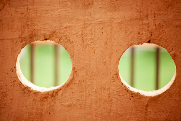 Two large holes in a wall, one on the left and one on the right. The holes are surrounded by a brown wall, and the view of the holes is partially blocked by a fence