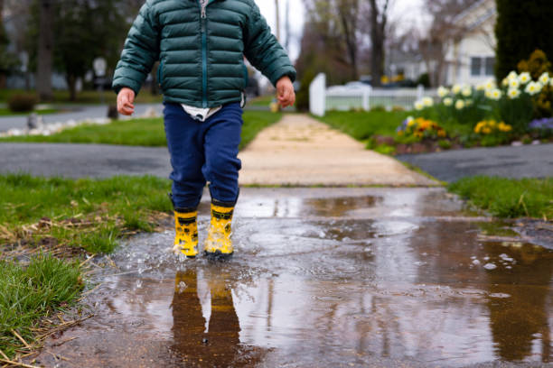 A toddler stomps and splashes in a puddle while wearing yellow rain boots A child in yellow rain boots plays and splashes in a puddle after a spring rain april showers may flowers stock pictures, royalty-free photos & images
