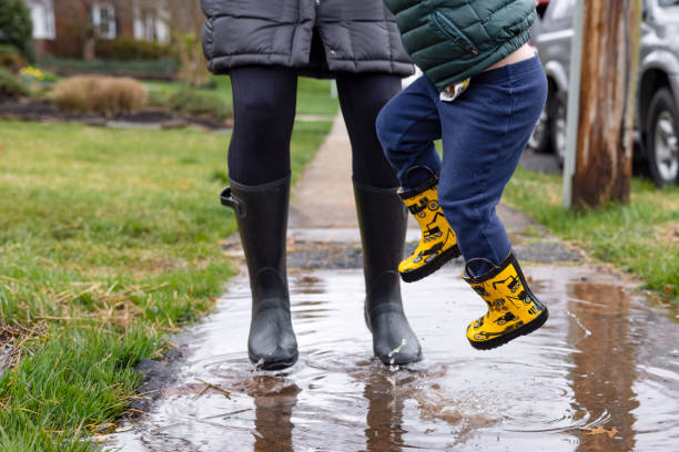Mom and Child Jump in Puddling While Wearing Rain Boots A mother and toddler in rain boots spash and play in a puddle after a springtime rain storm april showers may flowers stock pictures, royalty-free photos & images